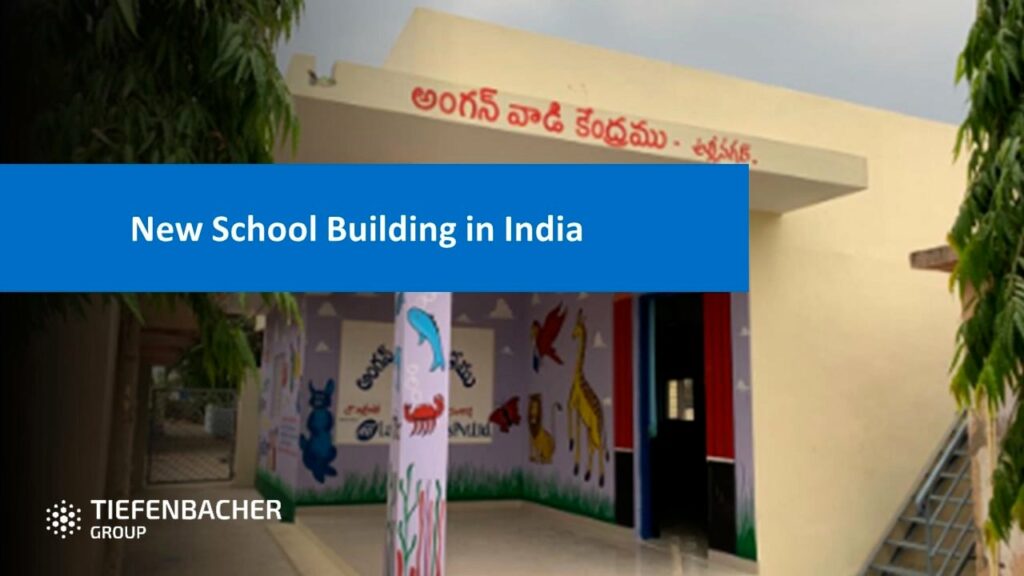 Tiefenbacher Group - A new school building in India features animal murals, a decorated pillar, and a Telugu sign above the entrance. A blue banner reads "New School Building in India." The TIEFENBACHER GROUP logo, representing a family-owned pharmaceutical company, is in the corner.