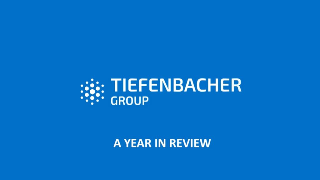 Tiefenbacher Group - White text on a blue background reads "Tiefenbacher Group" with a circular dotted logo to the left, highlighting "A Year in Review" and their commitment to pharmaceutical healthcare solutions.