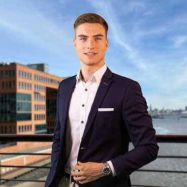 Lorenz Knoor standing on a balcony in a dark suit with a river and modern office buildings in the background.